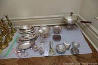 Wide view showing multiple silver plated trays, salt and pepper shakers, napkin rings, small vases, and a covered serving dish (chafing dish) with a handle.