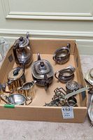 Lot of silver plate tea and coffee service items in a cardboard box, showing some wear and tarnishing.