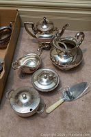 Overview of all silver plated items including teapot with stand, pitcher, gravy boat, two sugar bowls, lidded pot, and cake knife.