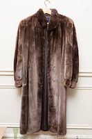 Full shot of the brown beaver fur coat hanging on a hanger, showing length and texture.