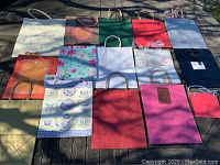 Photo showing 15 assorted gift bags on a wooden surface in natural light with various colors and designs.