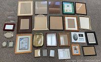 Clear photo showing an assortment of more than 25 picture frames laid out, featuring differing sizes and colors, rectangular and oval shapes.