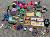 Photo of assorted small toys and craft items on carpet including balls, figures, modeling clay, origami paper, and accessories.