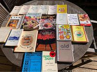 Photo of all 20 cookbooks and magazines arranged on a round table showing varying cover designs and colors.