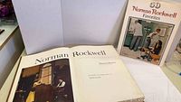 Open hardcover Norman Rockwell book showing title page 'Norman Rockwell Artist and Illustrator' and visible wear to pages and cover edges.