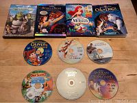 Photo showing DVD cases and discs laid out on table including Shrek, Beauty and the Beast, The Little Mermaid, Cats & Dogs, Oliver & Company, Tigger Movie, Captain Cameron's, Open Season 2, Flushed Away, The Indian Outboard.