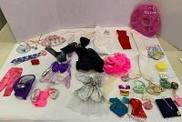 Full assortment of Barbie doll clothing and accessories arranged on a white background showing dresses, purses, inflatable pool raft, and small accessories.