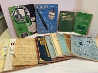 Photo showing 19 vintage music books and sheet music, including titles like Nick Mancoff Spanish Guitar, Mel Bay Method, Fifty Famous Favorites, Song Session, and various others with distinct early 20th-century cover designs and wear.