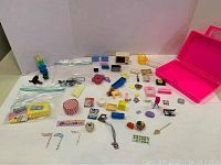 Photo showing the open pink Barbie box along with an assortment of small doll accessories including miniature furniture and fashion items.