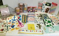Overview of scrapbooking supplies including patterned tapes, stickers, pencils, scissors, and decorative paper embellishments arranged on a table