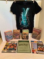 Photo showing four Harry Potter paperback books with some wear, a black t-shirt with Harry Potter and Voldemort graphic, and several coloring pages laid out on a table.