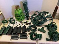 Lot overview showing various sizes of dark green heavy duty electrical cords, several 3-outlet power strips in green and black, and adapters arranged on a flat surface