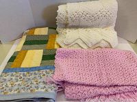 Three folded blankets: white knit baby blanket, Winnie the Pooh patchwork blanket, and pink knit blanket.