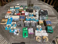 Wide top-down photo showing all assorted hardware items spread out on wooden table, including various packaged screws, locks, switches, and hinges.