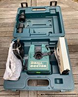 Open drill bit sharpener unit with cord, accessories, and case interior shown on wooden surface.