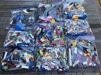 Nine resealable plastic bags filled with assorted LEGO pieces in multiple colors and shapes, displayed on a wooden surface.