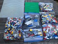 8 bags of assorted LEGO bricks in various colors and 2 flat baseplates arranged on a wooden surface.