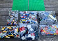 Photo showing 7 plastic bags of assorted LEGO bricks in multiple colors and 2 large green baseplates