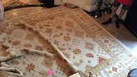 Full view of the rug spread on the floor showing the southwestern Aztec pattern, warm beige base with rust and gold accents, and fringe at edges.