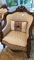 Front view of vintage Victorian style arm chair with white diamond patterned upholstery, carved and gilded wood frame, and decorative pillow.