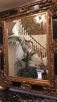 Front full view of the large wall mirror showing the reflective surface and carved wooden frame with gold and black accents.