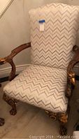 Front view of chair showing white chevron patterned upholstery and carved walnut wood arms and legs with gold leaf detail.