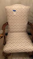 Front view of the upholstered chair showing the chevron patterned fabric upholstery and top of the carved wooden armrests.