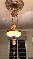 Full view of the hanging chandelier showing the brass ceiling mount, chains, ornamental crown, and alabaster shade lit up.