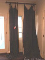 Full view of two long dark-colored drapes hanging from curtain rod in front of window, showing full length to floor.