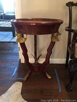 Front view of gilt tripod tray table showing red wood finish and gold eagle head accents on legs with eagle figurine at base.