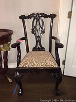 Front view of wooden armchair showing carved backrest and leopard print upholstery.
