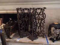 View of antique style metal fireplace guard with ornate floral cutout design, standing upright in front of fireplace opening