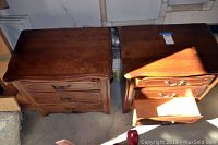 Overhead view of two walnut nightstands side by side, one drawer opened showing interior light wooden finish, brass handles visible.