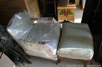 Wrapped chair and ottoman set in muted green fabric, wood carved legs, seen from side angle.