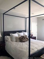 Dark bamboo four poster canopy bed assembled and made up with white bedding in a well-lit bedroom.
