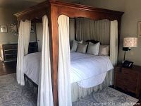 Assembled canopy bed in a styled bedroom showing walnut finish and white sheers