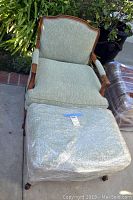 Chair and ottoman set shown outdoors with detailed wooden frames and light green upholstery.