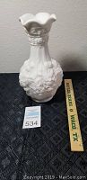 White Doeskin ceramic vase with floral relief detail on the body, placed beside a 12-inch ruler for size reference.