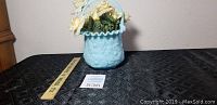 Blue satin glass Fenton basket with poppy pattern and handle, artificial flowers inside, shown on a black patterned surface with measuring ruler for scale.