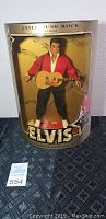 Front view of the Elvis Presley Jailhouse Rock doll in original box with visible gold and black themed packaging and doll wearing red outfit holding guitar.