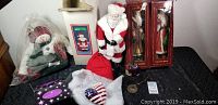 Photo showing collection of Christmas decorations including Santa Claus figurines, snowman, and various ornaments on a black tablecloth.