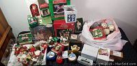 Wide shot of loose and boxed Christmas decorations including Lennox figurine boxes, various boxed ornaments, loose ornaments in a plastic bag, nutcracker figurines, and miniature holiday collectibles.
