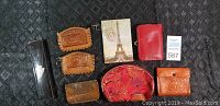 Photo showing all items laid out on a dark patterned surface: eyeglass case, various leather wallets, pouch with Eiffel Tower print, red coin purse, orange wallet.