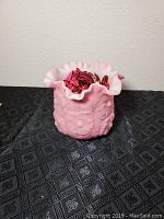 Front angled view of satin pink Fenton vase showing ripple edge and poppy pattern, vase filled with dried petals.
