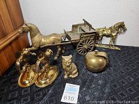 Photo showing all brass decorative items on black patterned cloth including horses, cart, apple container, owl, candle holders.