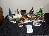 Christmas scene table decor items arranged on a black table, showing multiple small figures, Christmas trees, a festive train, and snow-covered bases.