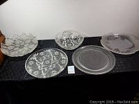 Five glass and crystal platters arranged on a black cloth showing various decorative cuts and patterns.