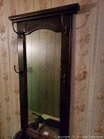 Front view of tall wooden hall tree with central mirror and metal hooks