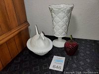 Photo showing three glass decor items: Fenton style milk glass hen covered dish, a white hobnail milk glass vase, and a red glass apple.