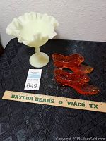 Yellow satin Fenton glass compote and orange glass shoe pair on black surface with measuring ruler